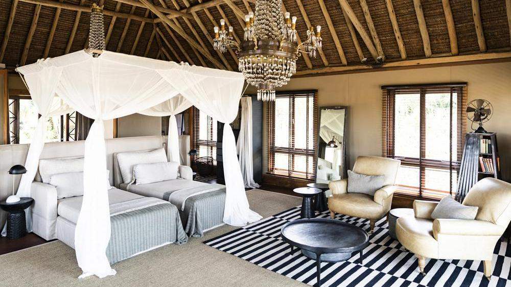 Twin beds with white canopy netting beneath a crystal chandelier, next to a seating area with leather armchairs.