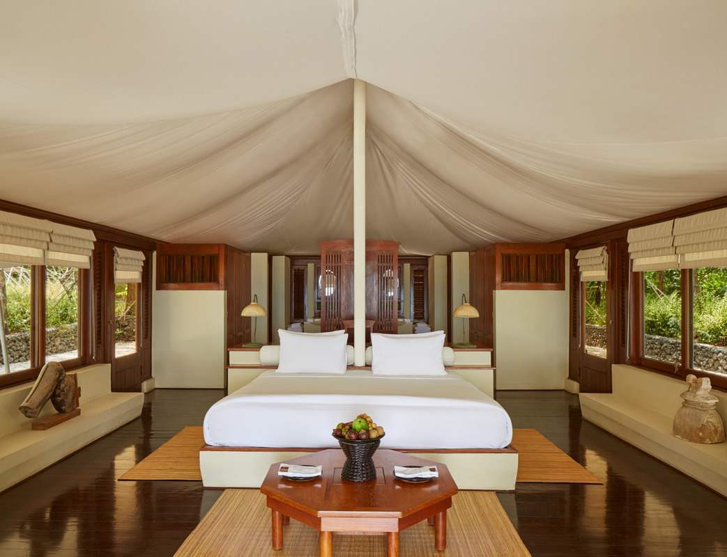 Symmetrical view of a luxury tent interior at Amanwanawith a white bed, wooden accents and soft draped ceiling fabric.