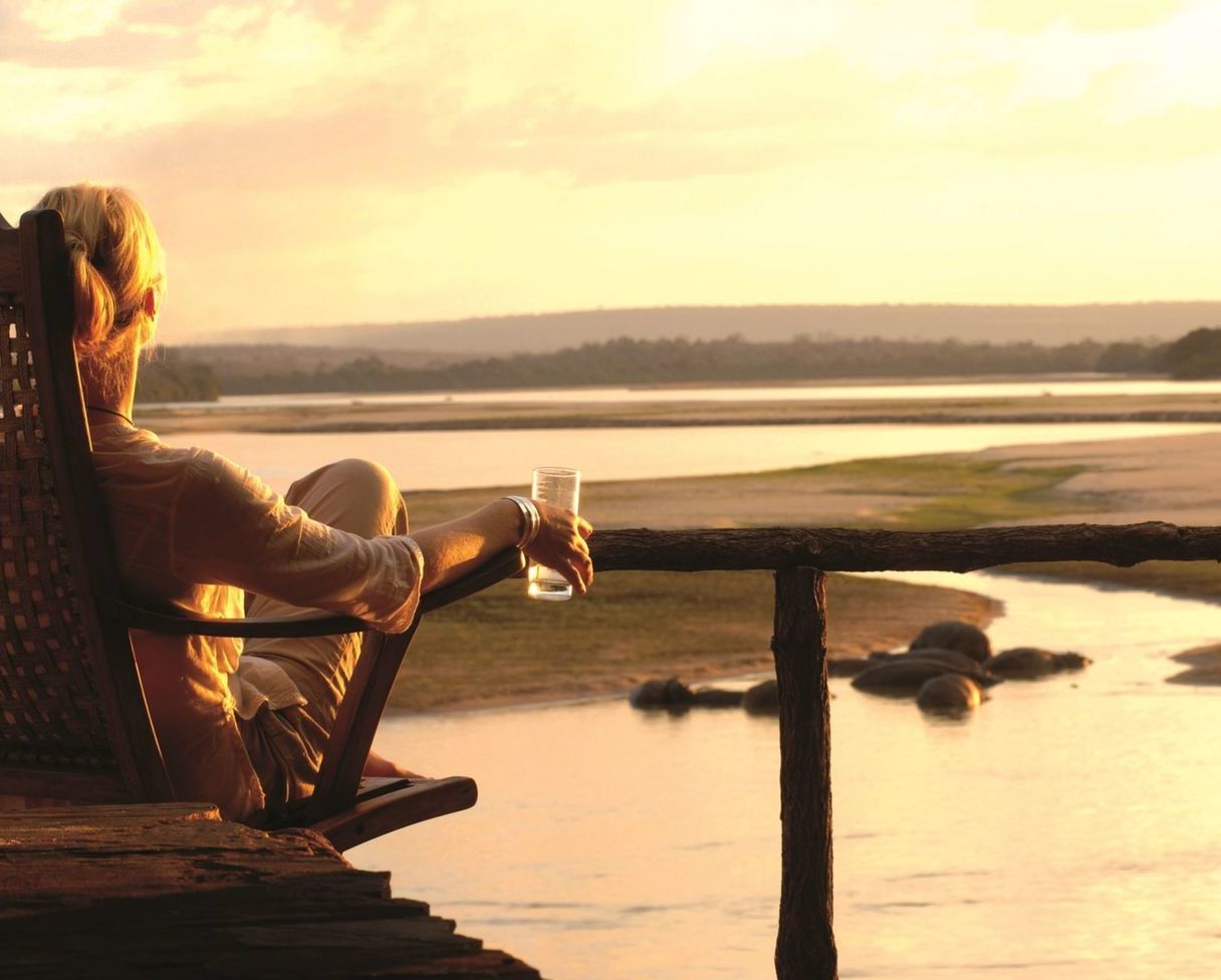 Woman enjoying a sundowner overlooking the Rujiji River on a panoramic terrace at Sand Rivers. at