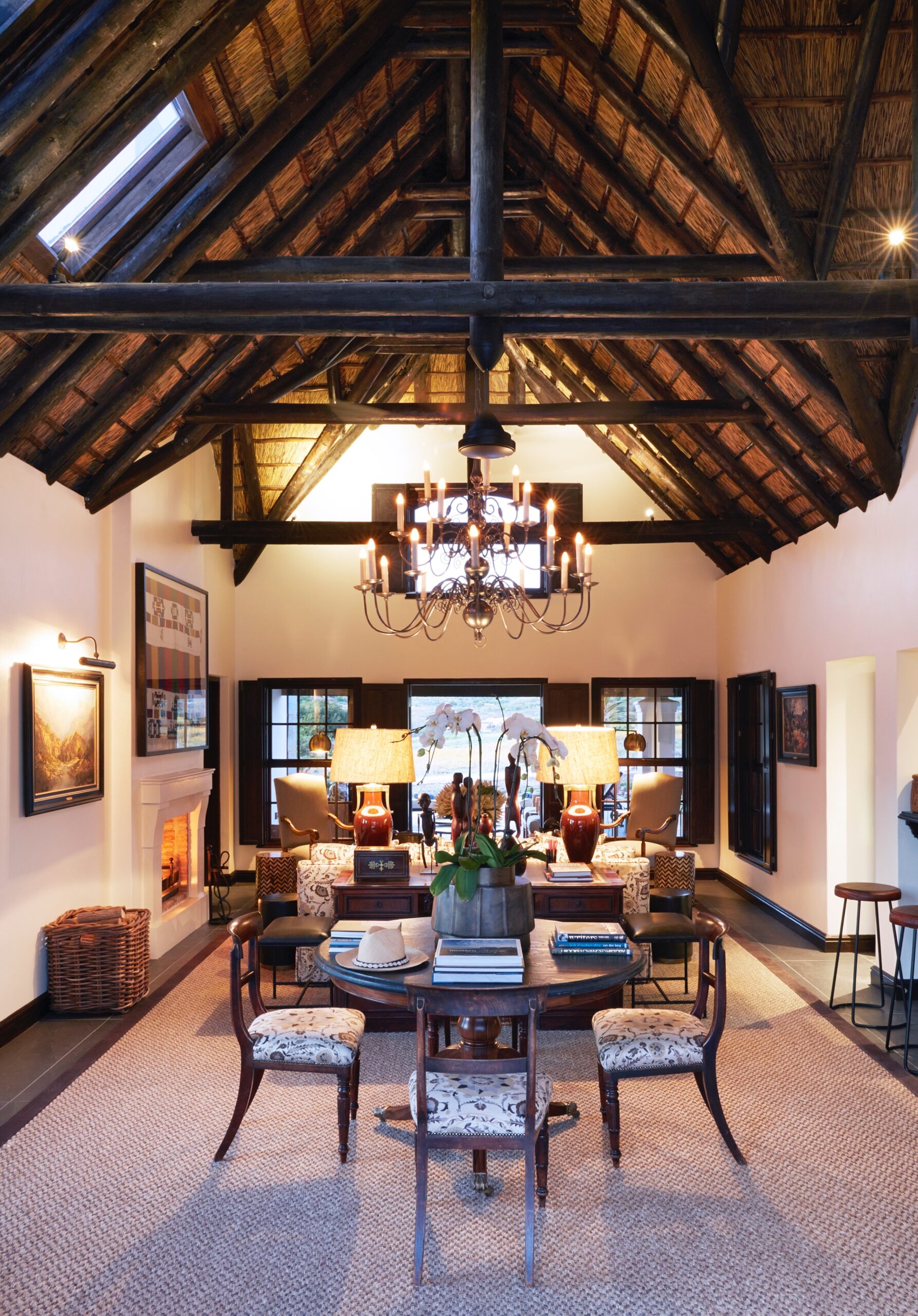 Elegant living room with high wooden beamed ceiling, chandelier, and a lit fireplace.
