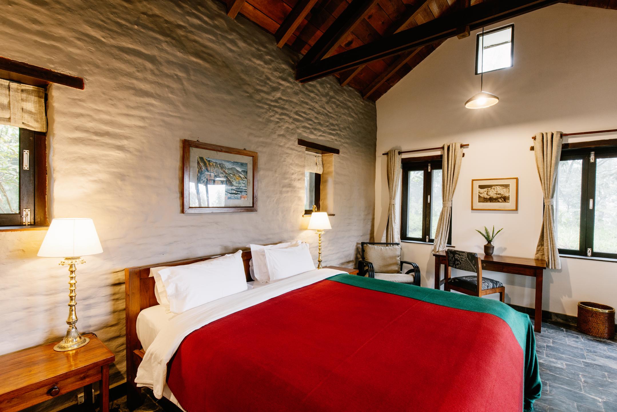 Cozy bedroom with a double bed, red coverlet, exposed beams, and framed art on walls.
