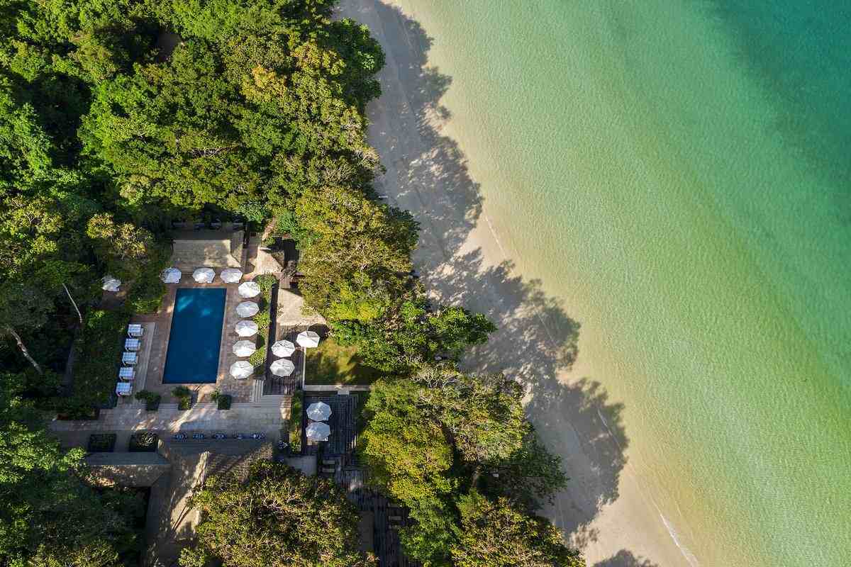 Bird's-eye view of the Datai's pool area located between a dense forest and the ocean shore.
