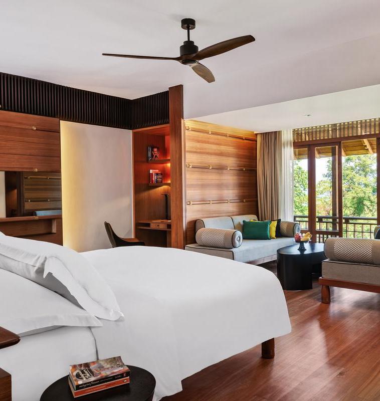 A bedroom at the Datai with wooden walls, white linens, a ceiling fan and a seating area.