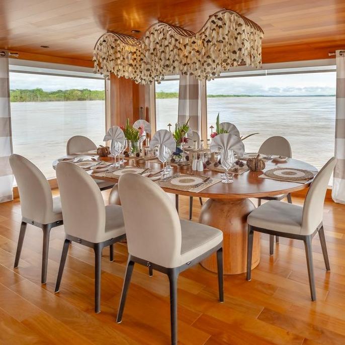 Formal dining table with white chairs and an ornate shell chandelier inside Delfin Ioverlooking the water.