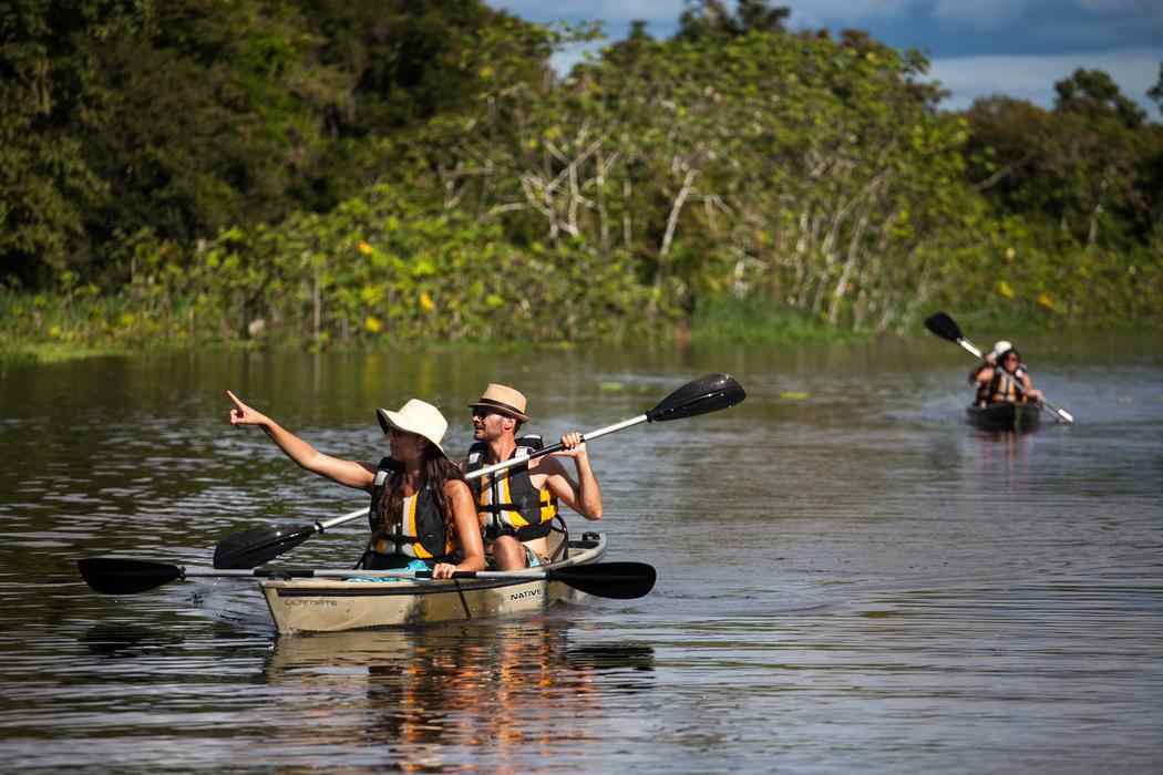 Two people kayaking on a river during a cruise excursion with a second kayak visible in the background.