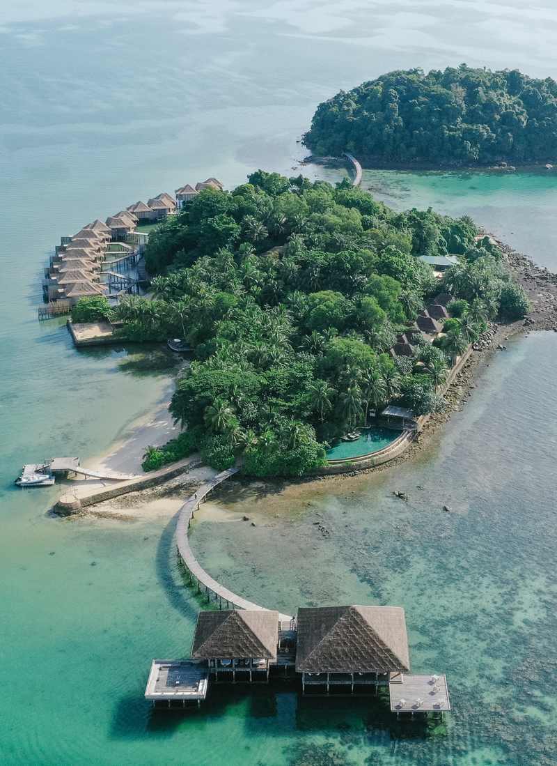High-angle view of a tropical island with thatched-roof villas built over the turquoise water.