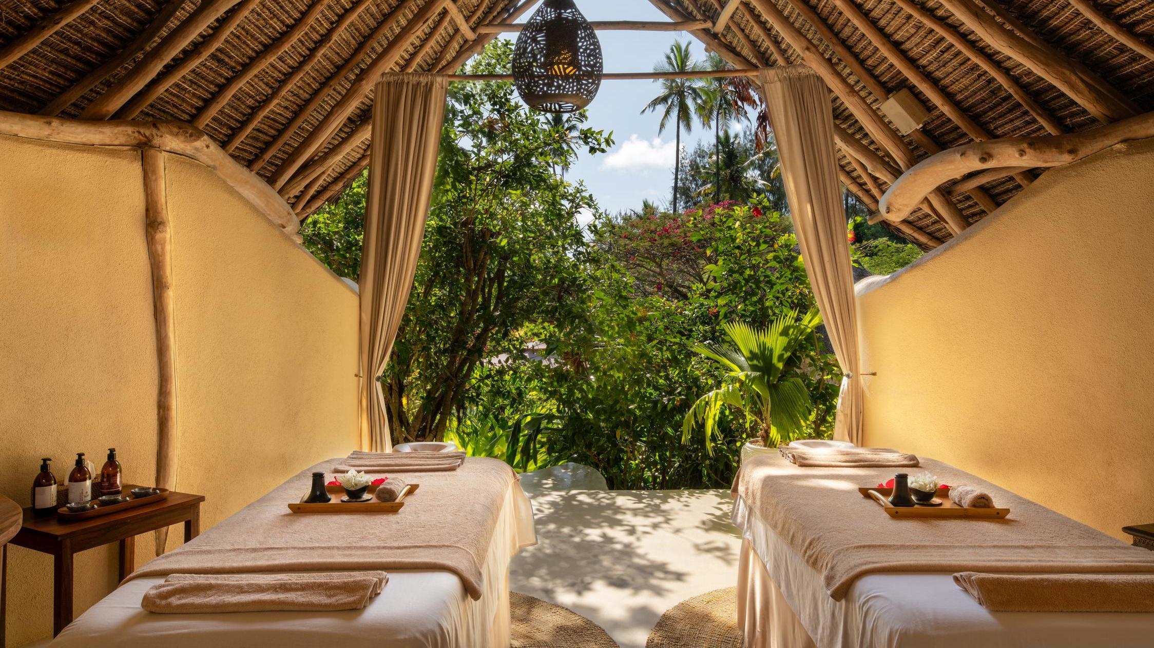 Open-air spa setup with two massage beds overlooking lush greenery.