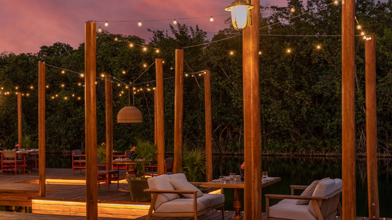 Outdoor deck with string lights at twilight, overlooking a tranquil water body.