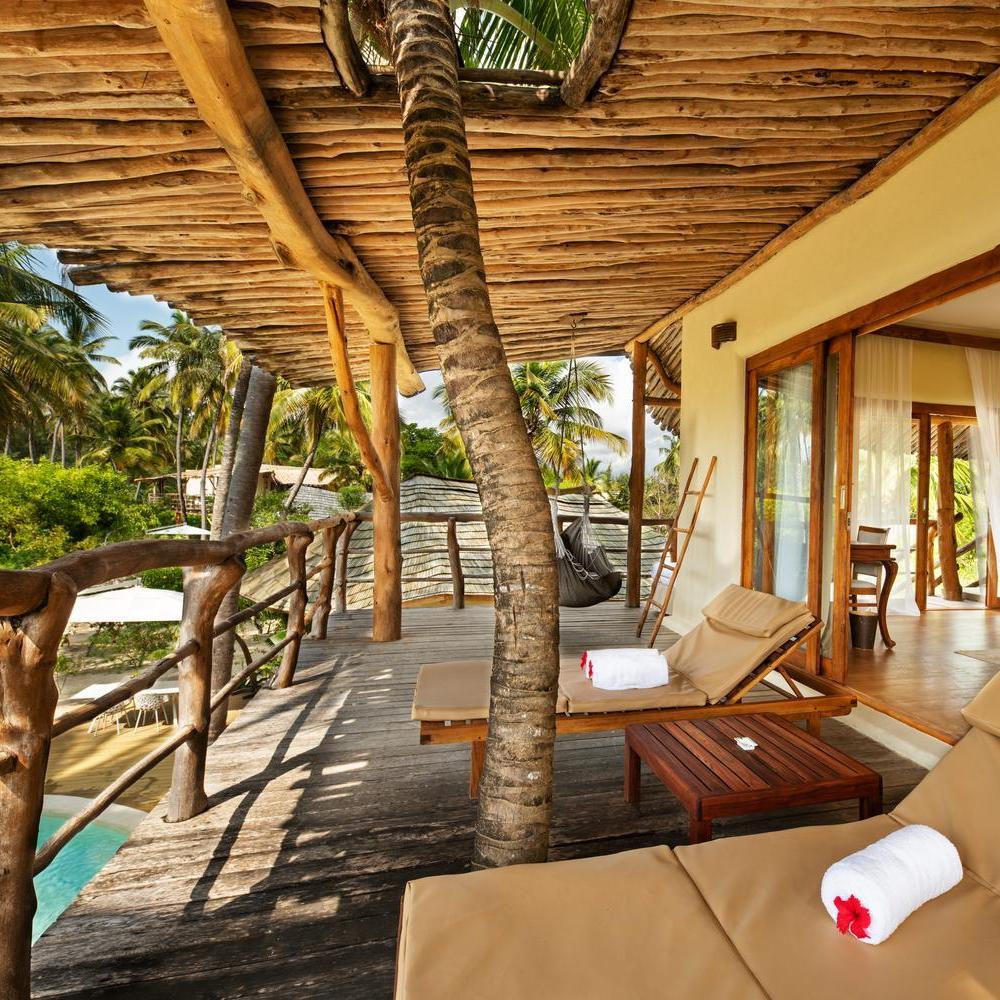 Tropical resort deck with hammock, sun loungers, and a palm tree integrated into wooden architecture.