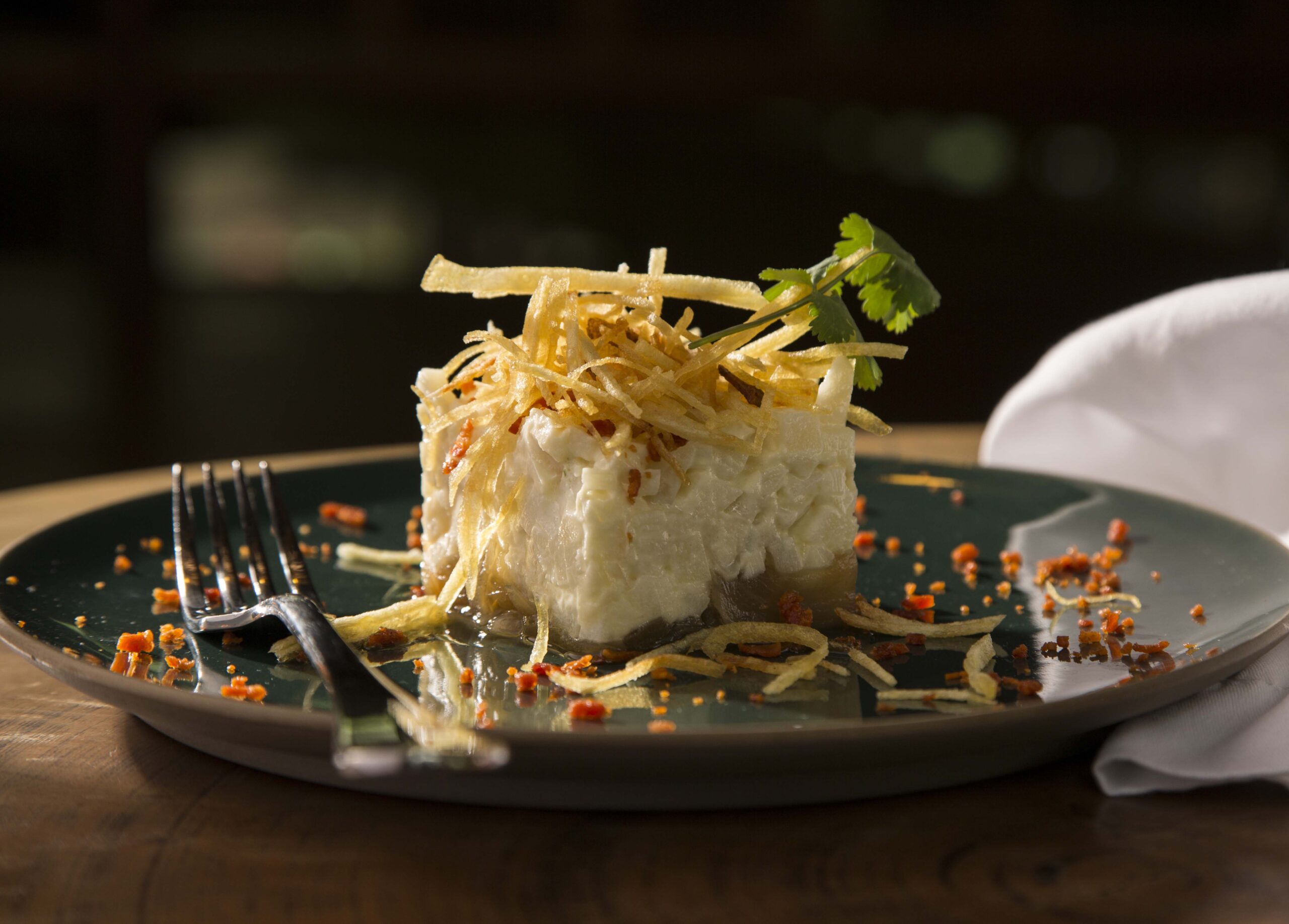 Gourmet dish with crispy potato topping on dark plate with fork.