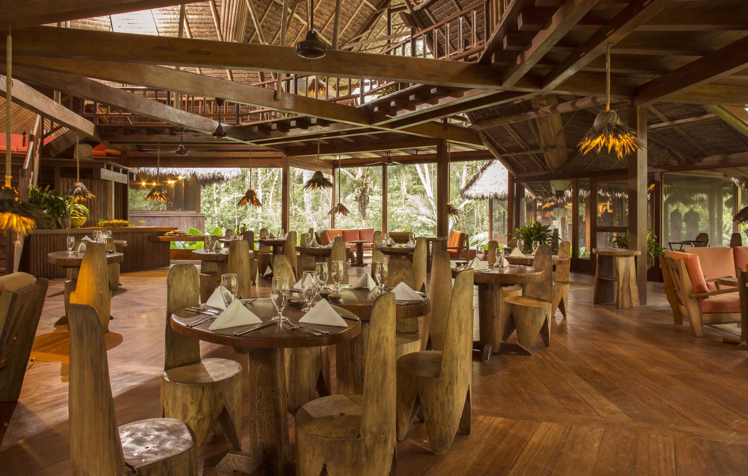 Rustic dining room with wooden furniture and tropical forest view through large windows.