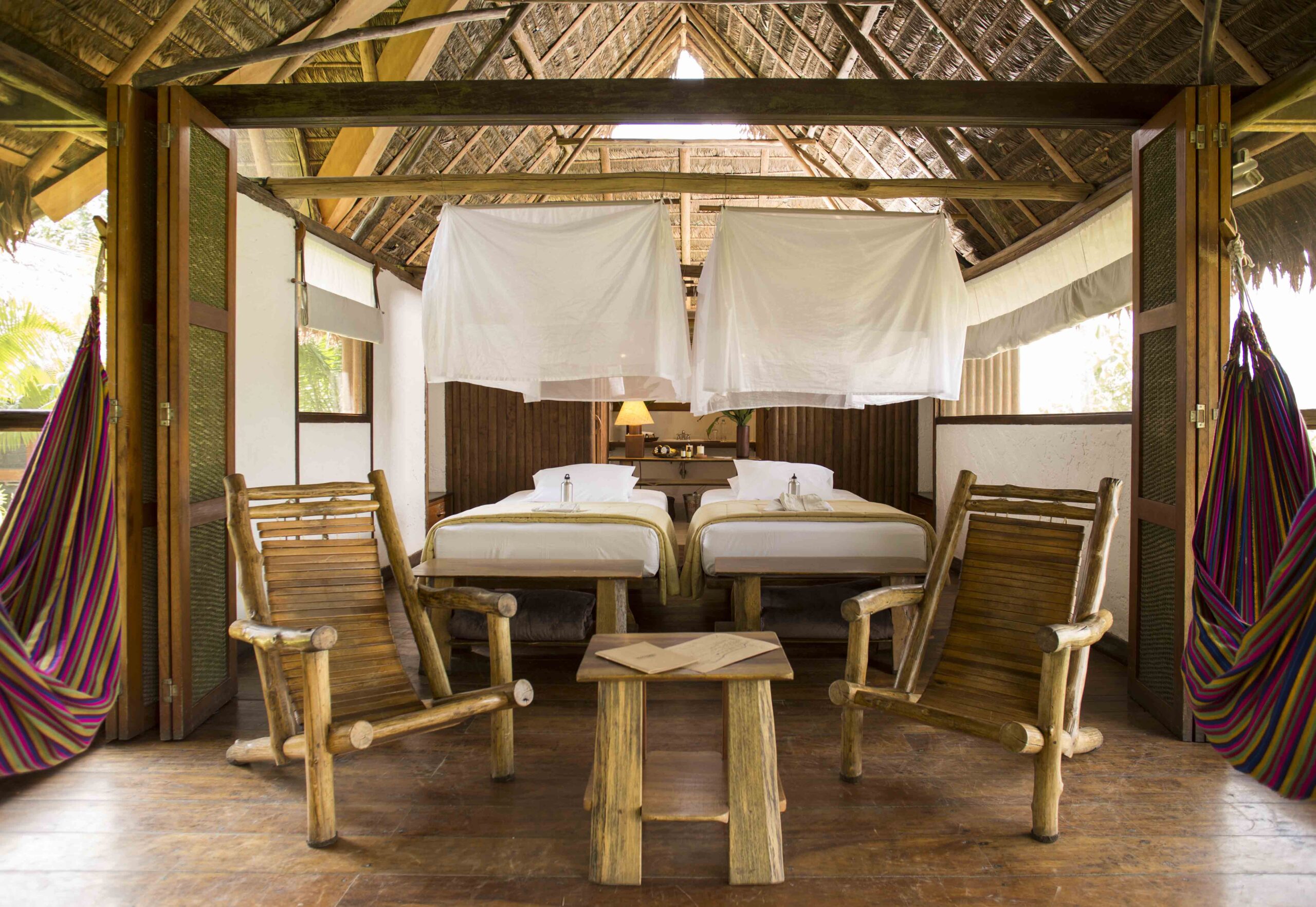 Rustic tropical bedroom with two beds, wooden furniture, and a striped hammock.