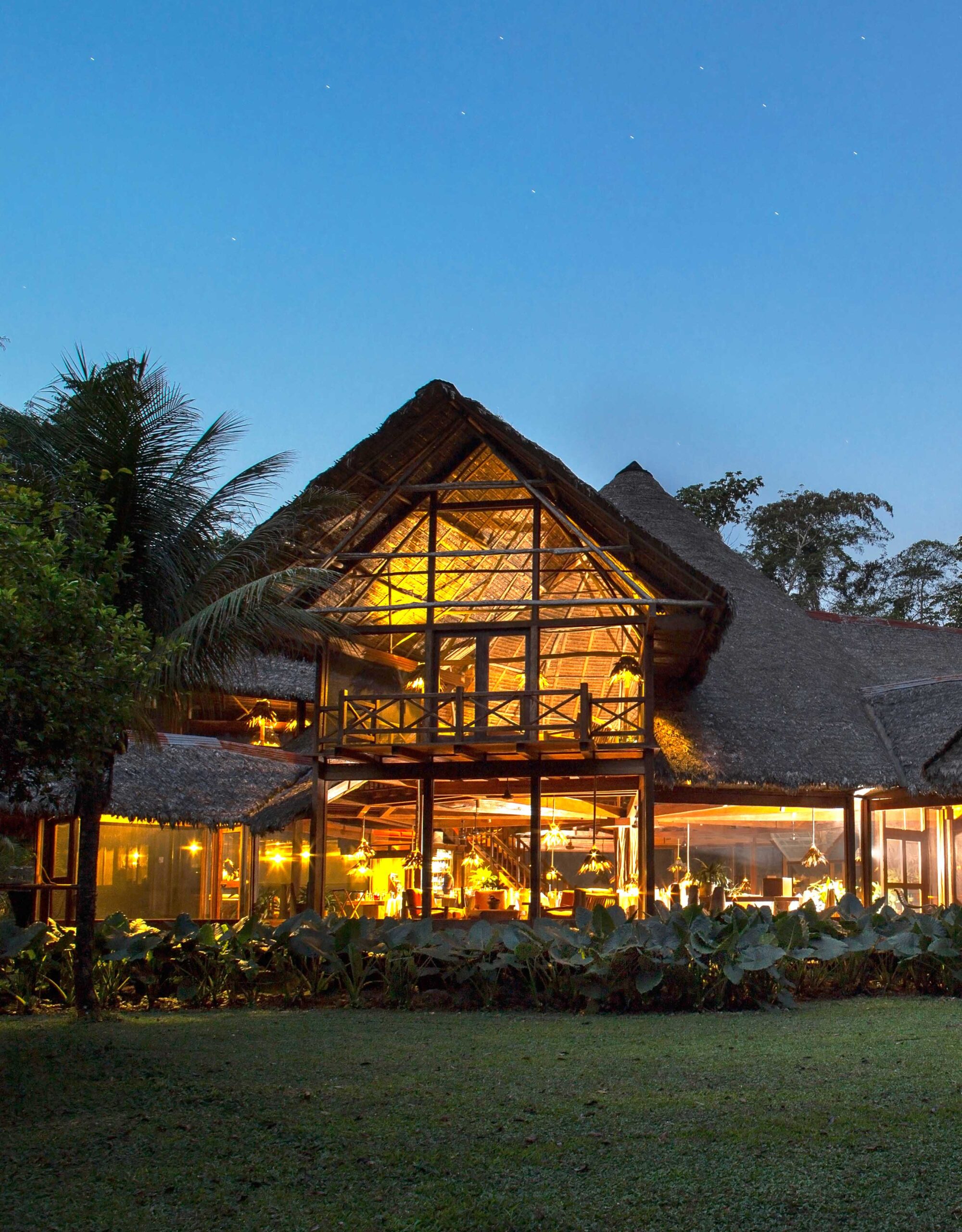 Thatch-roofed lodge illuminated at twilight with a starry sky above.