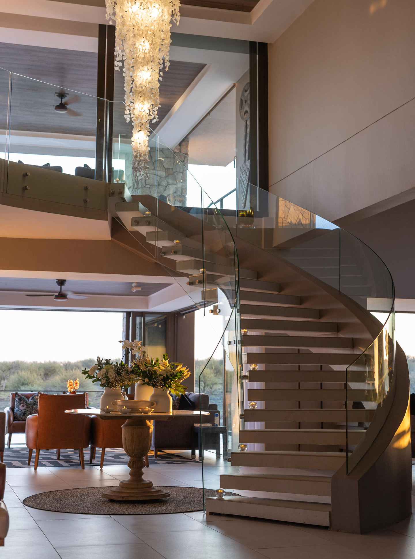 Modern interior with spiral staircase, glass balustrade, and elegant chandelier.