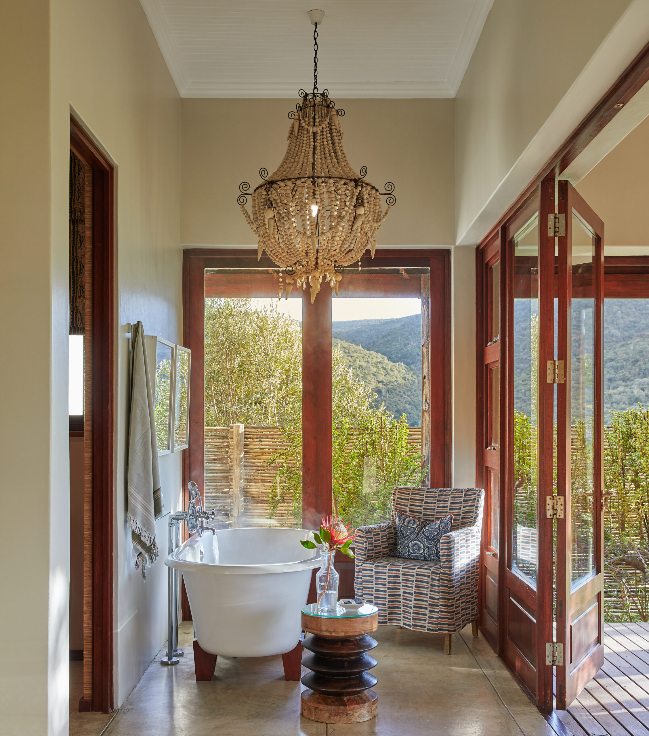 Luxurious bathroom with a freestanding tub and chandelier, opening to a scenic view of nature.
