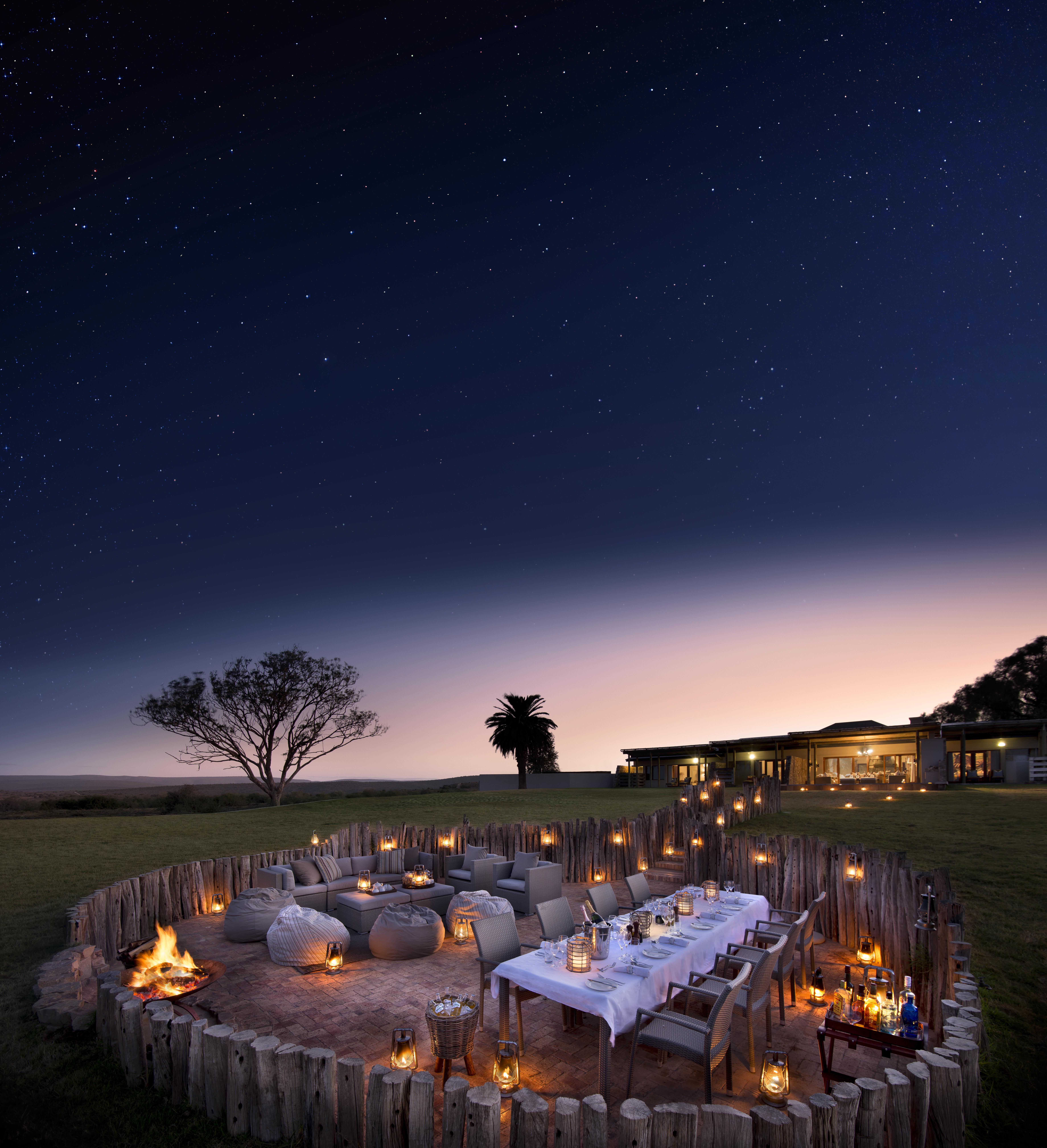 Outdoor dining area with lit candles under a starry sky, next to a building.