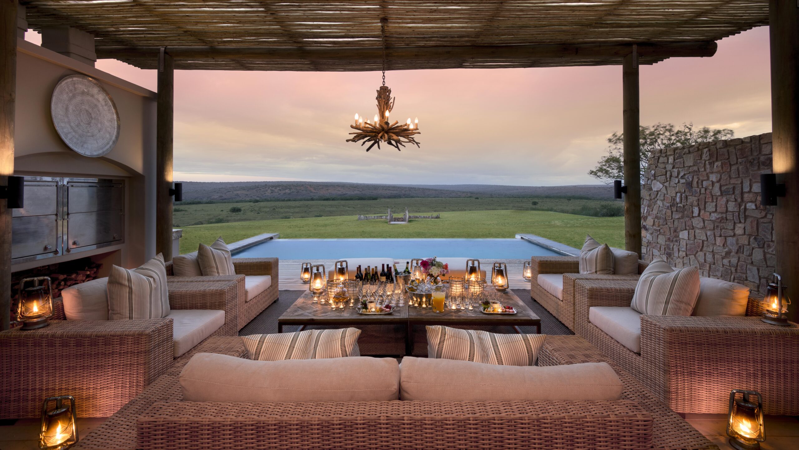 Luxury outdoor lounge overlooking a serene landscape at dusk, with elegant dining setup and pool.