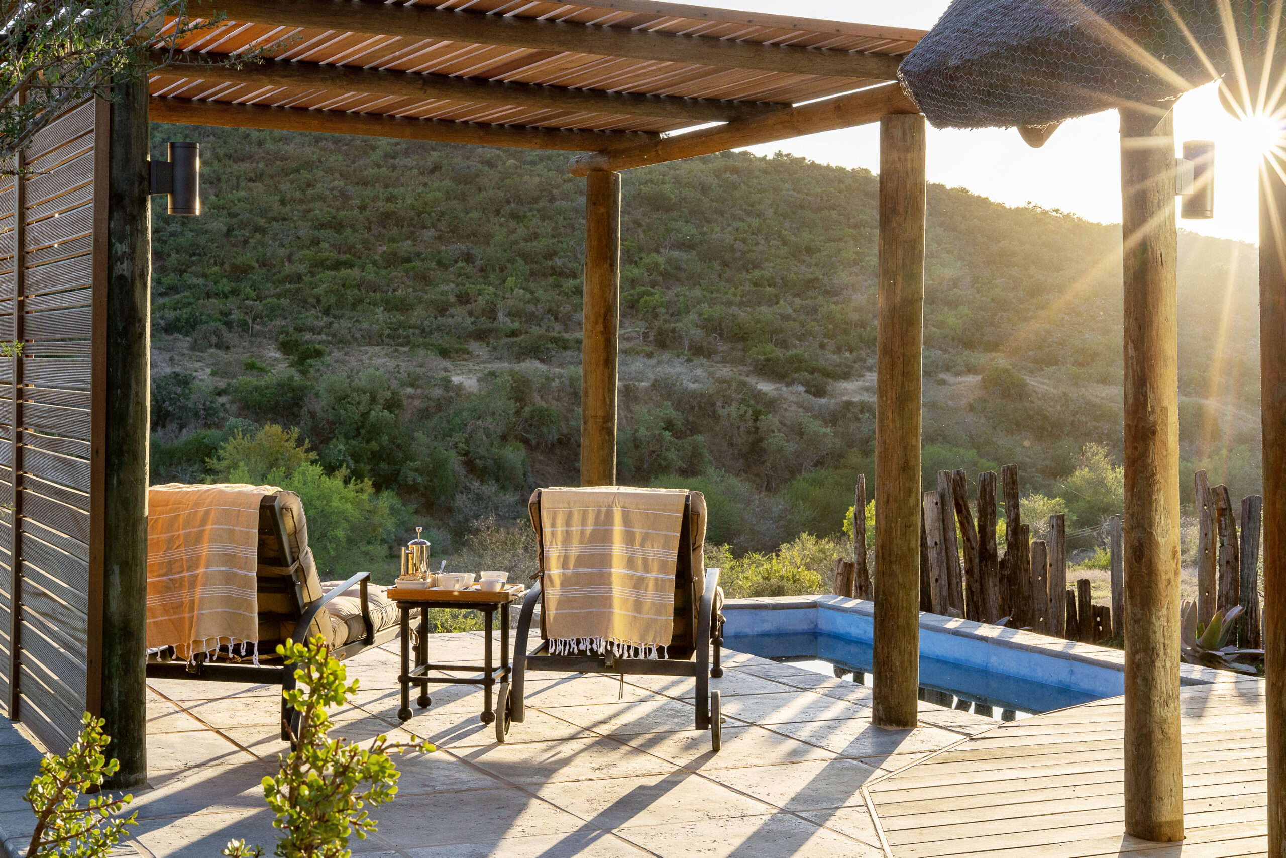 Sunny outdoor patio with chairs, a table set for two, and a scenic hill view.