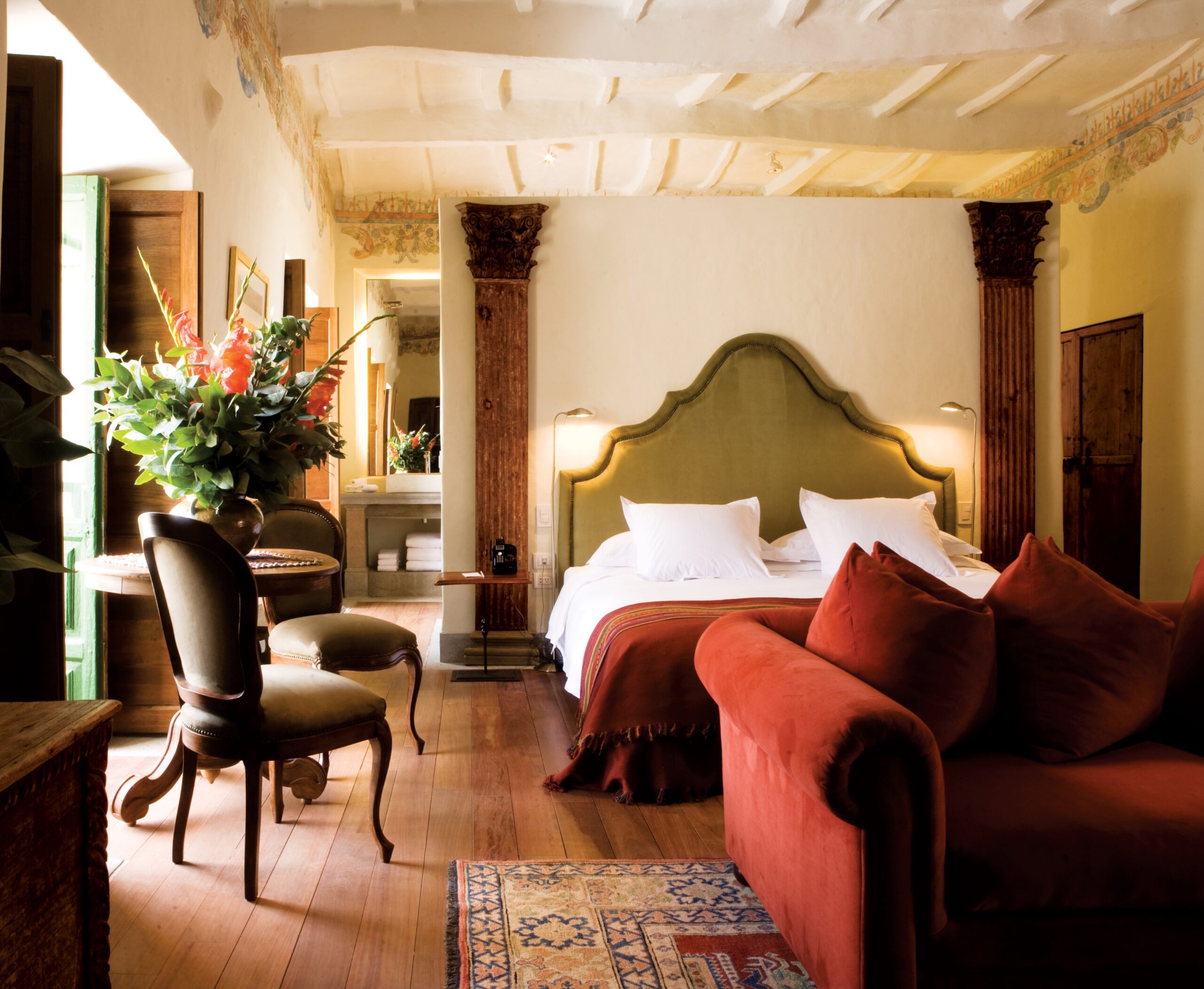 Elegant bedroom with a large bed, red sofa, antique furniture, and decorative ceiling.