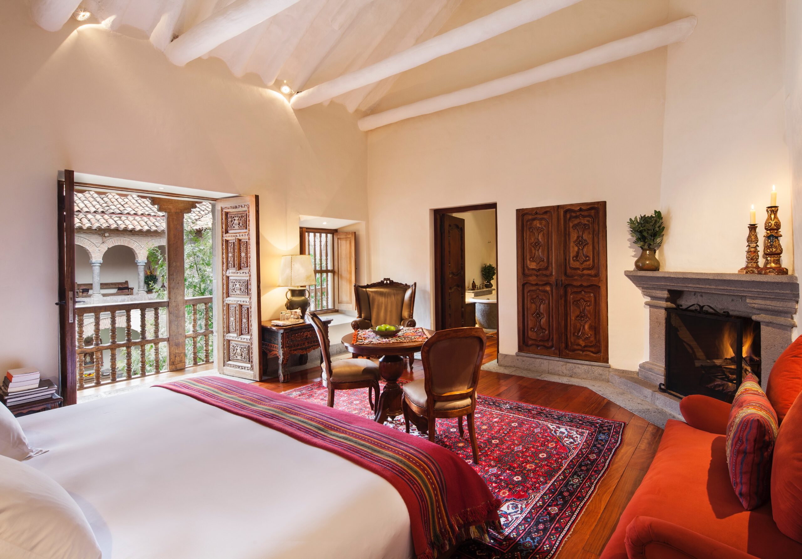 Elegant bedroom with fireplace, traditional decor, and balcony overlooking a courtyard.