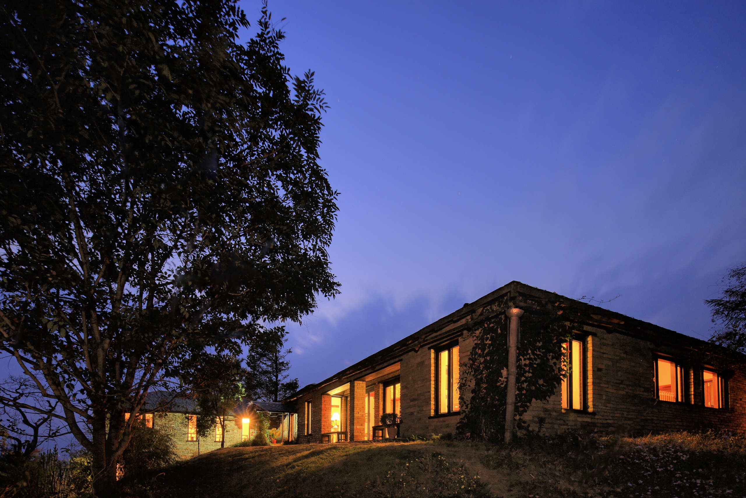 Illuminated brick house at dusk with a blue sky and wispy clouds.