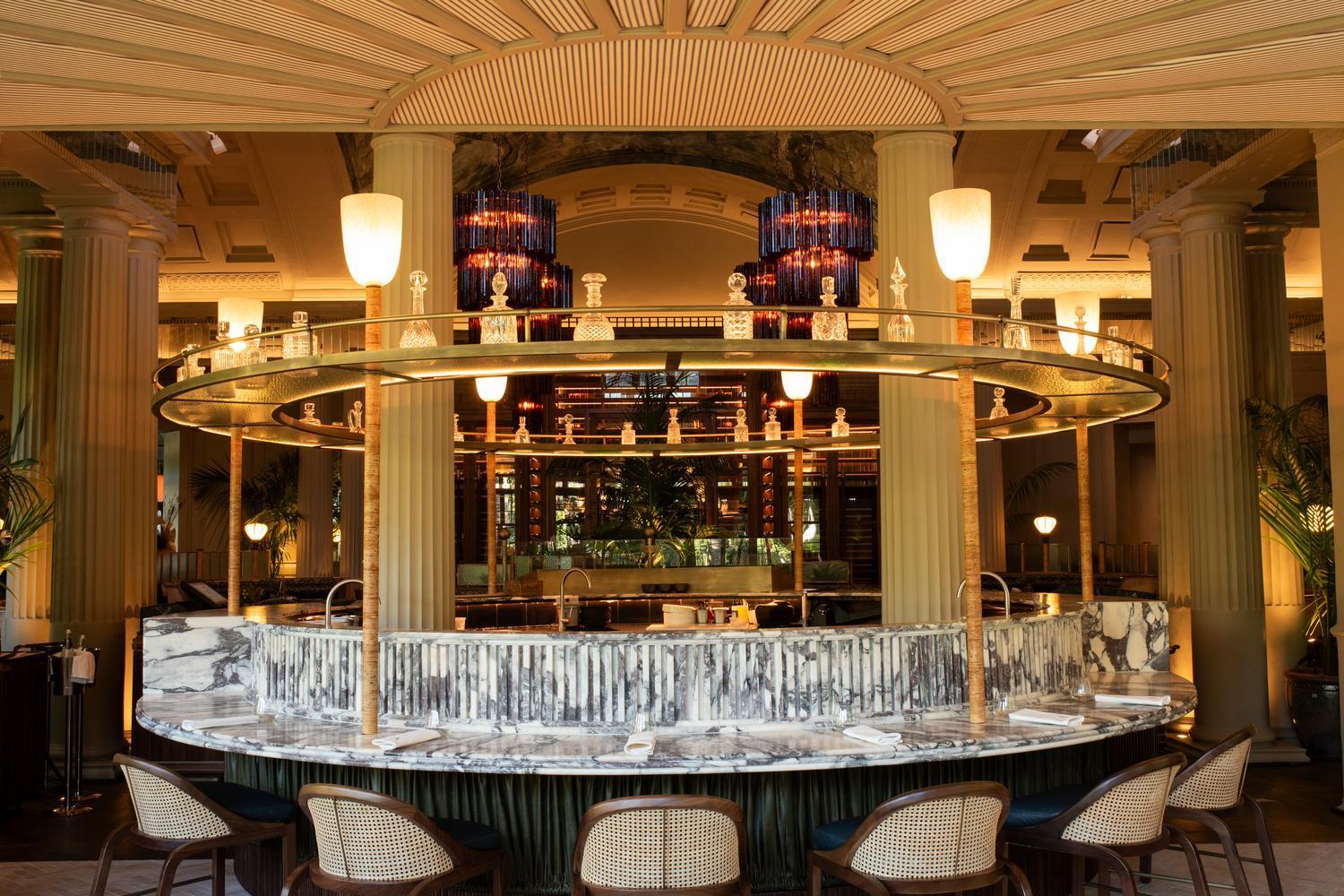 Sophisticated circular bar with a marble base, wooden chairs, and tiered glass shelving inside the Mount Nelson.