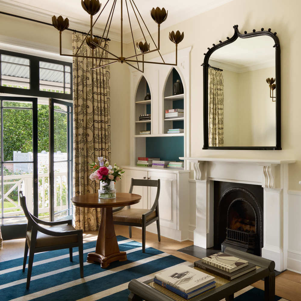 Classic hotel suite interior with a fireplace, arched mirror, and a small dining table over a blue striped rug.