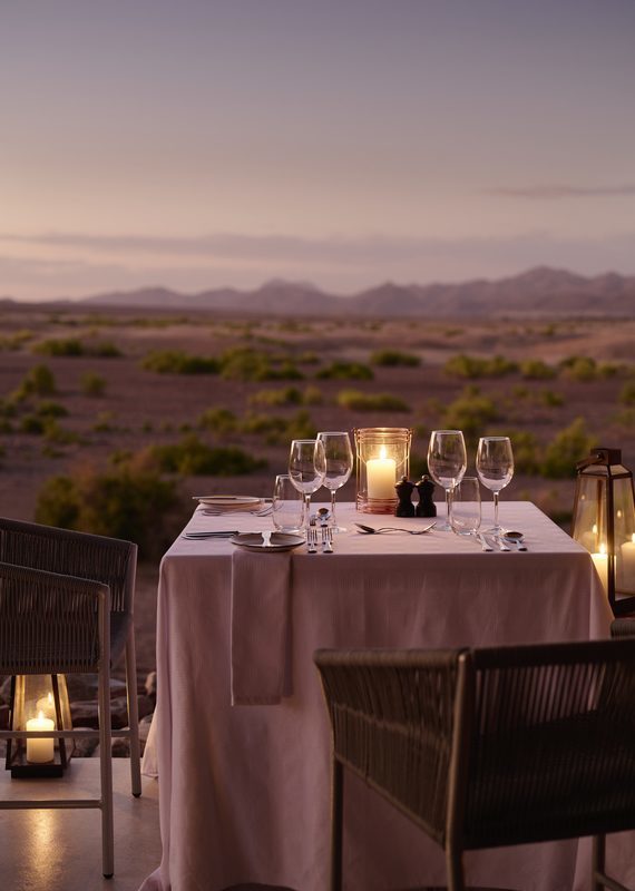Candlelit table for two set for dinner on a patio overlooking a vast desert landscape at dusk.