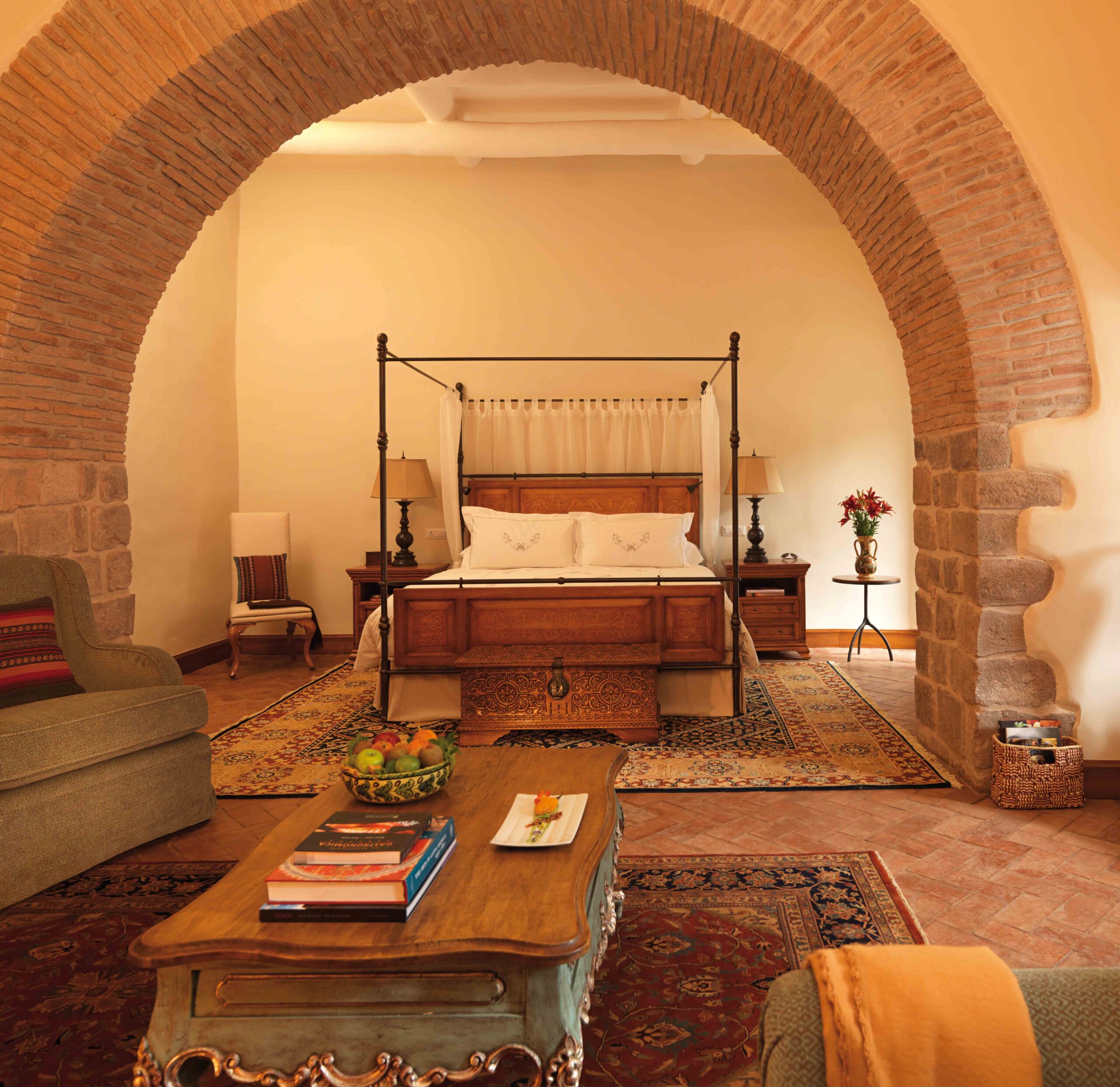 Elegant bedroom with a four-poster bed, arched brickwork, warm lighting, and traditional decor.