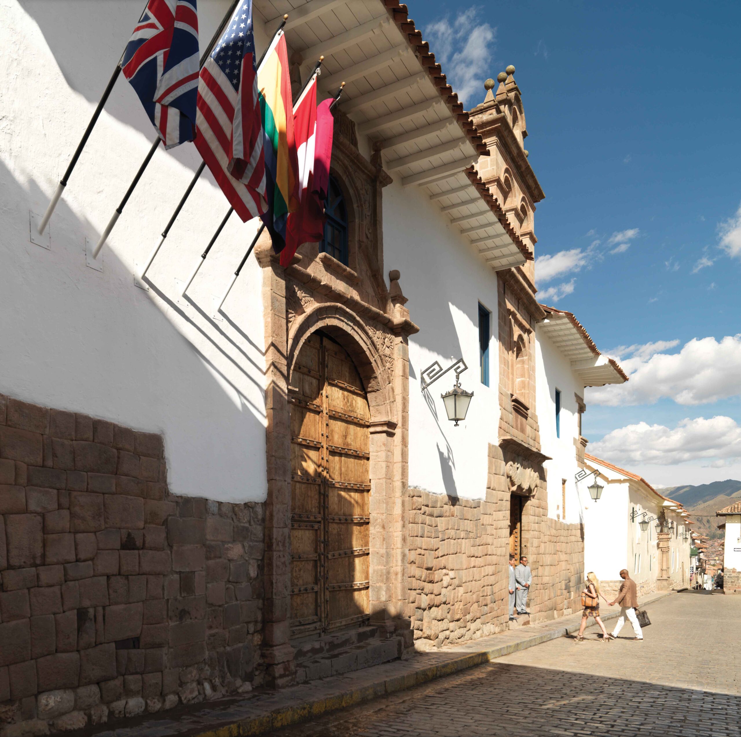 Colonial building with international flags, cobbled street, and pedestrians in sunlight.
