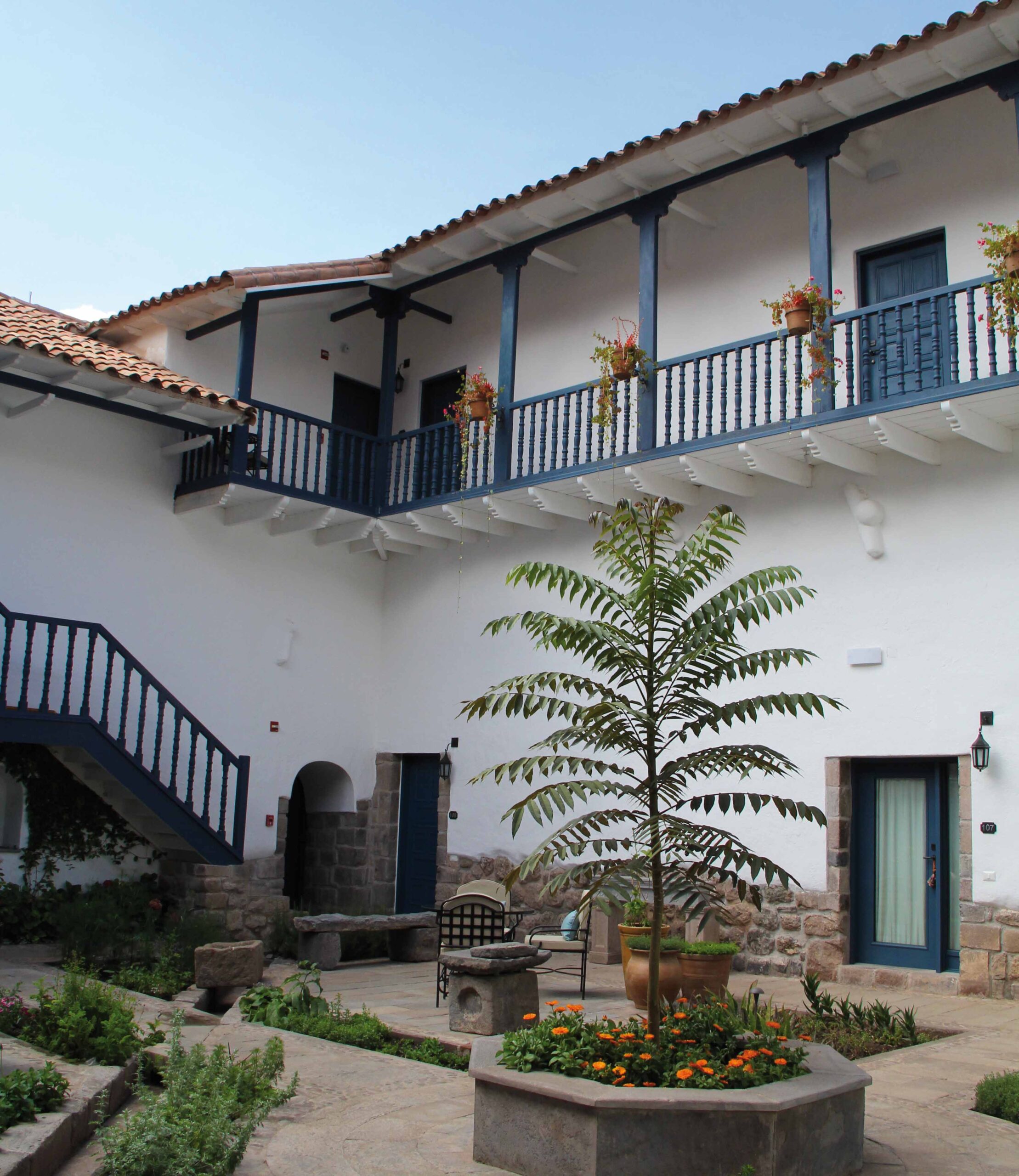 Traditional white building with blue balconies, staircases, and a central courtyard with plants.