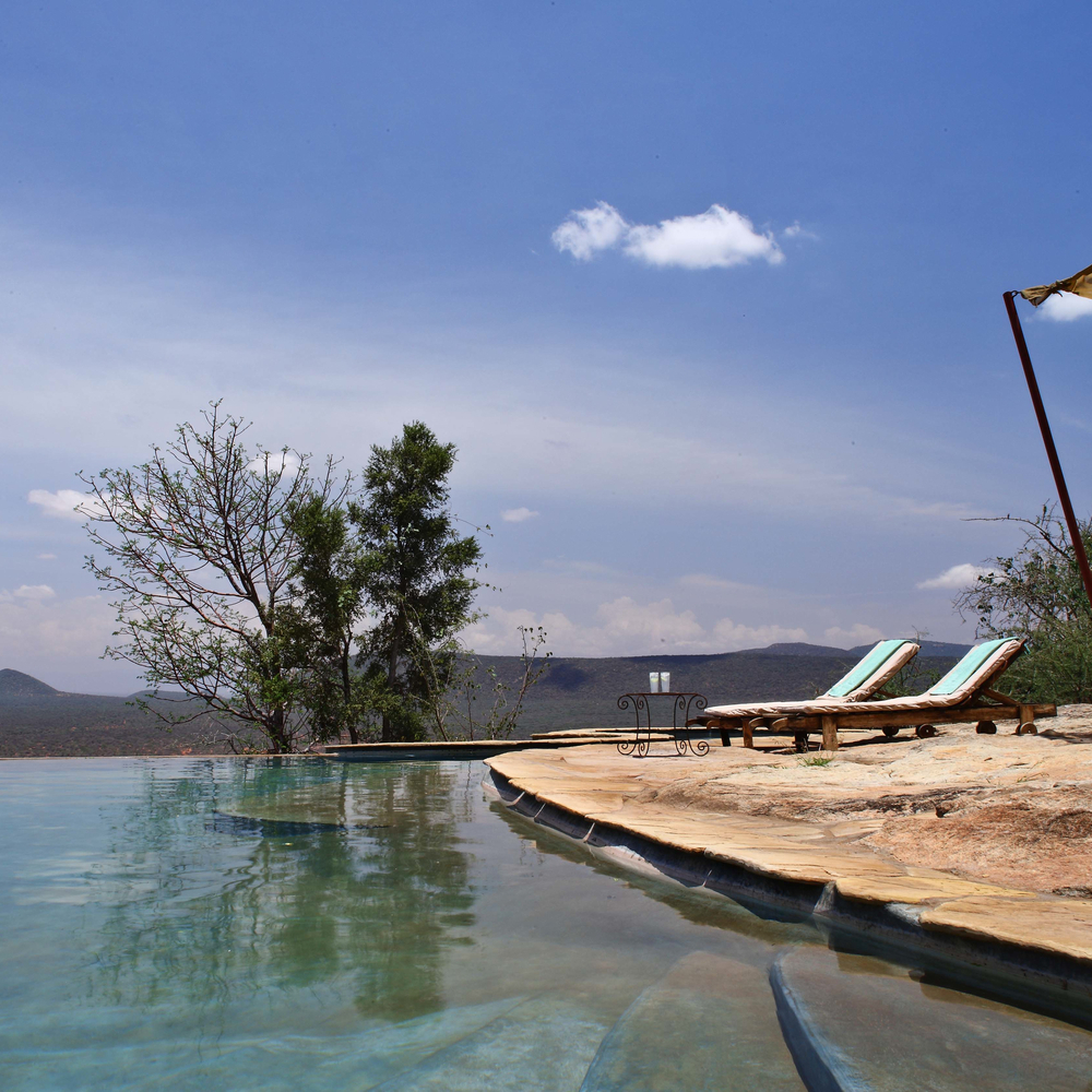 Sun loungers on a stone deck next to a calm swimming pool overlooking the Samburu landscape.