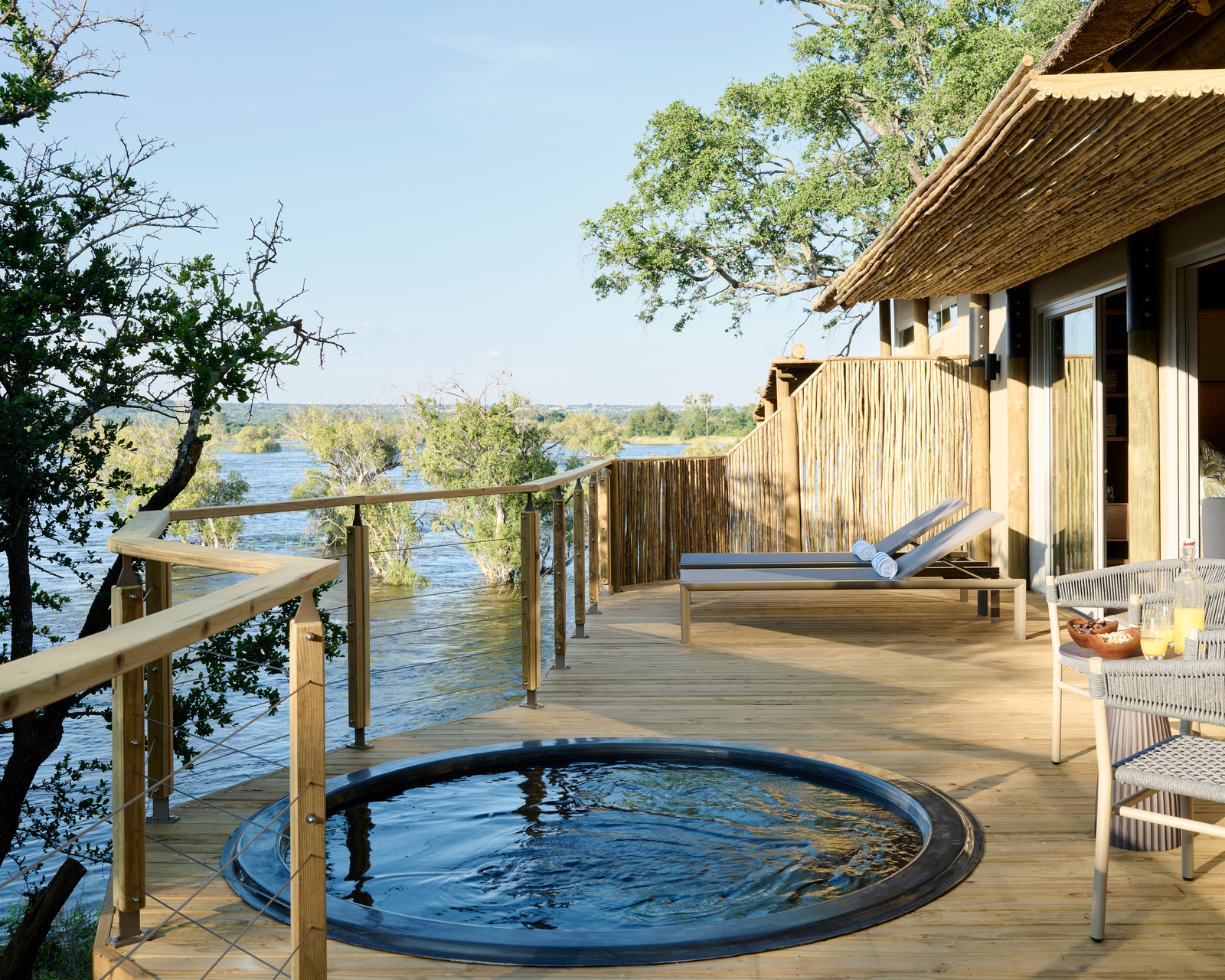 A circular plunge pool on a wooden deck with lounge chairs overlooking a river at Victoria Falls River Lodge.