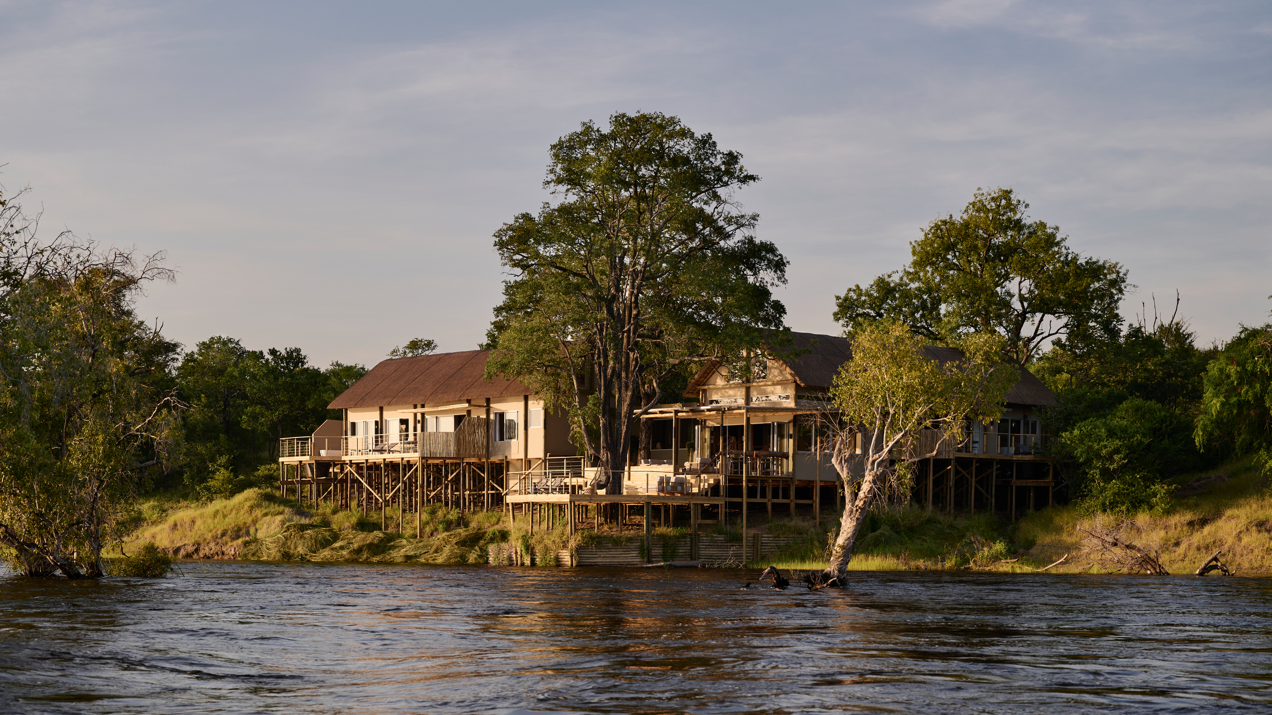 Exterior view of a waterfront villa on stilts at Victoria Falls River Lodge during the golden hour.