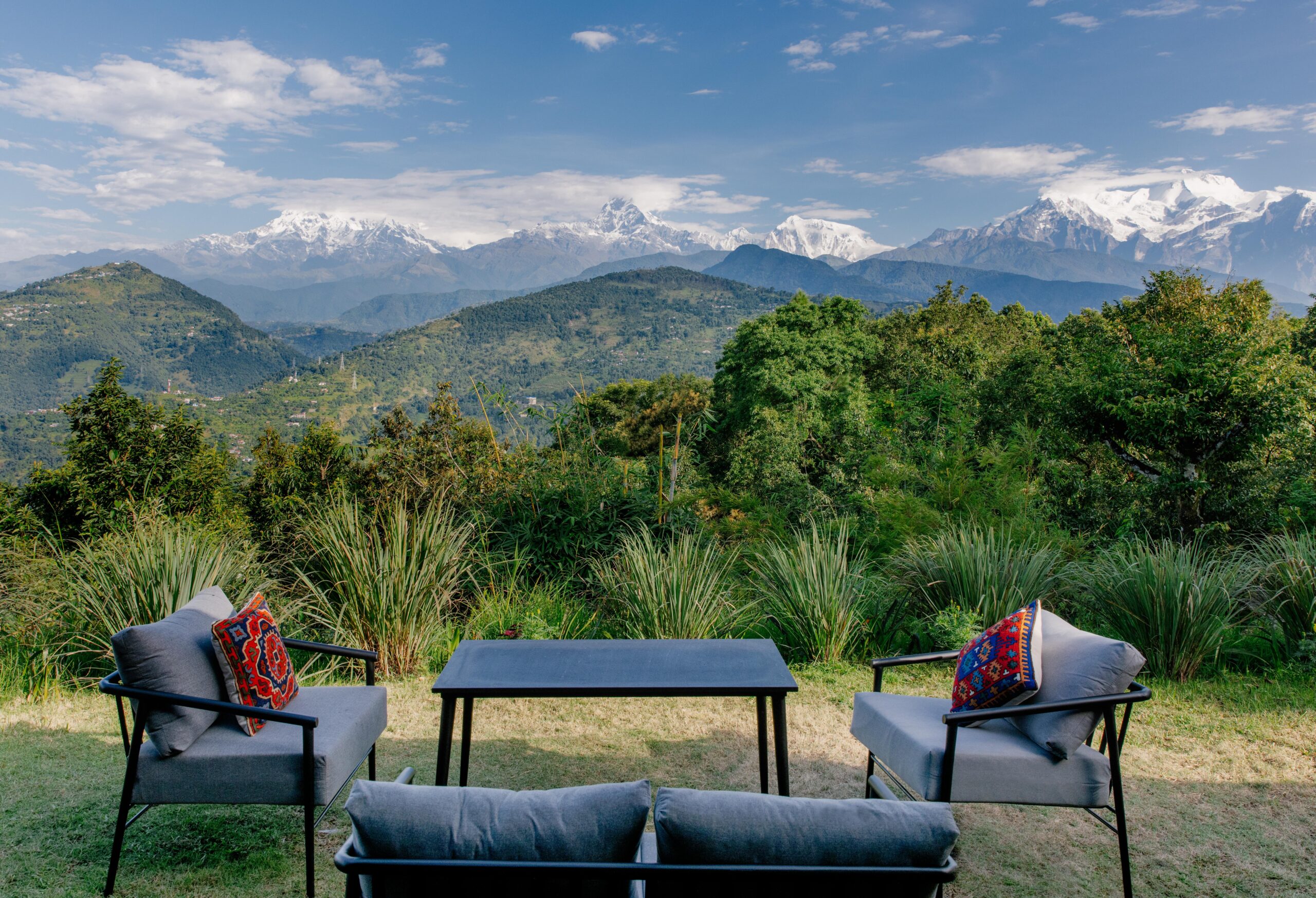 Outdoor seating area with a view of snow-capped mountains and green hills.