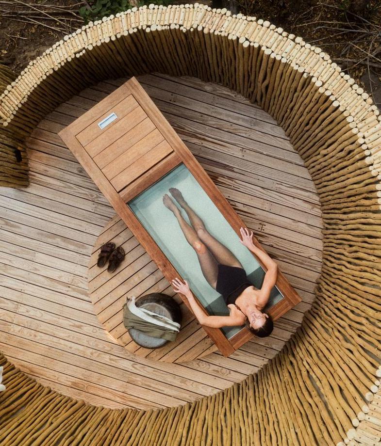 Aerial view of. awoman in an outdoor bath surrounded by bamboo circular walls at The Sanctuary spa at Wilderness Mombo