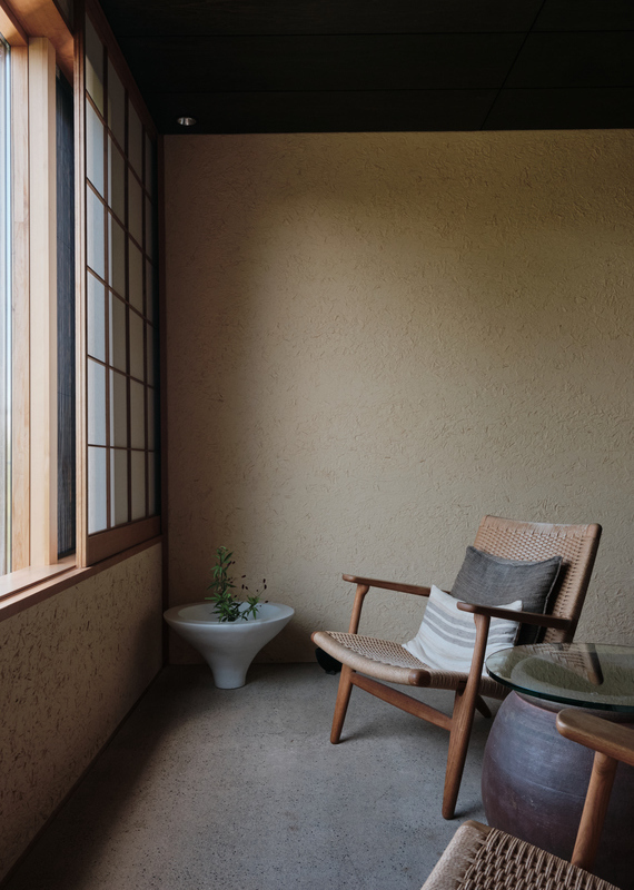 A minimalist Zen suite seating area with a wooden chair, a side table, and a white plant bowl by a paper screen window.