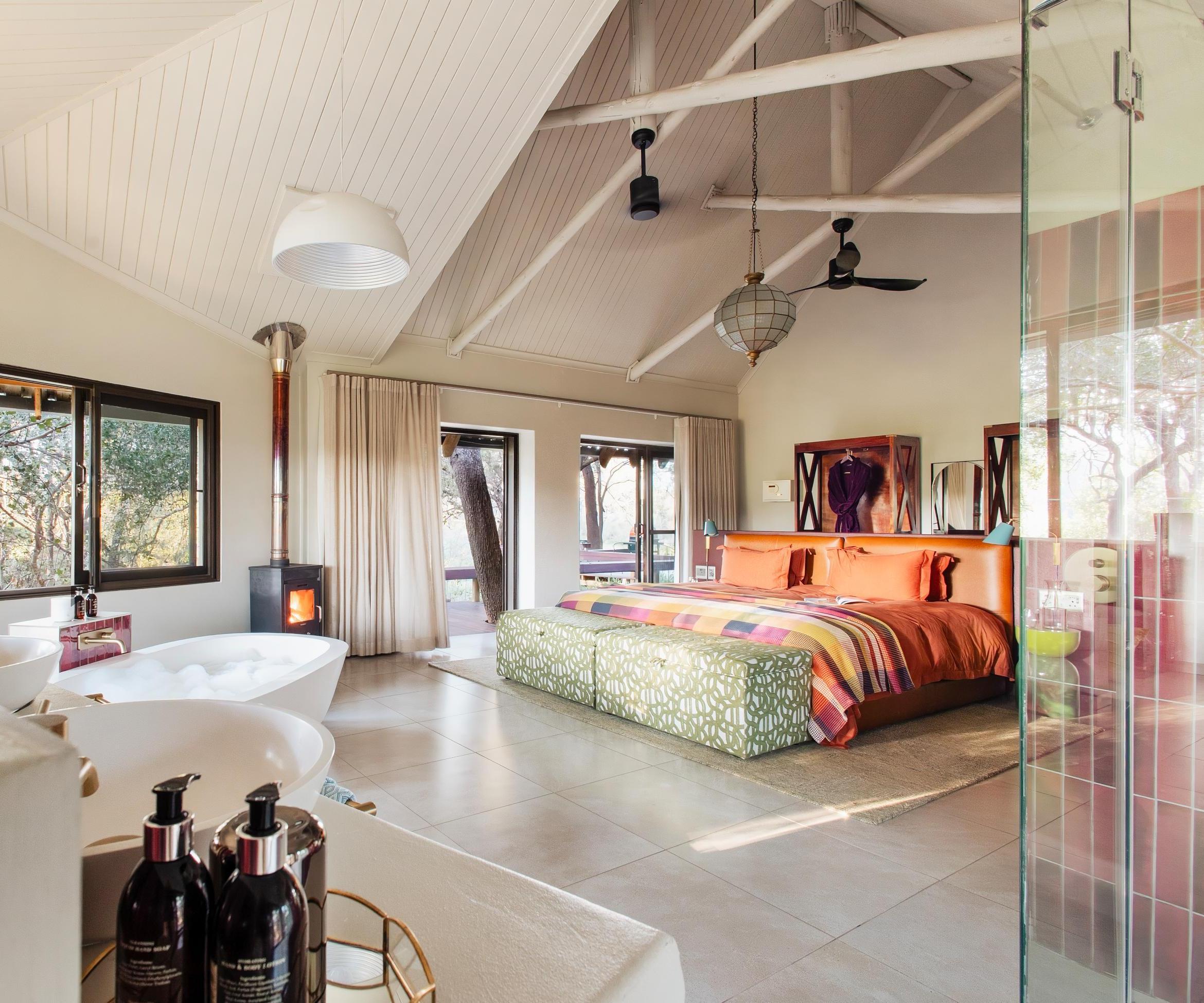 Spacious bedroom at Jaci's Private Lodge with a brightly colored bed, a white bathtub, and large scenic windows.