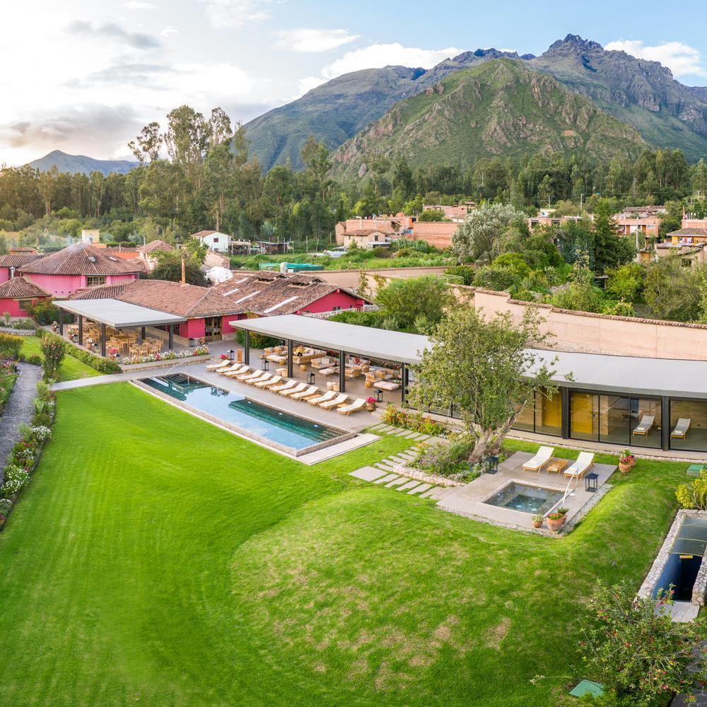 Aerial view of a resort with a long swimming pool, green lawns, covered patio, and red buildings.