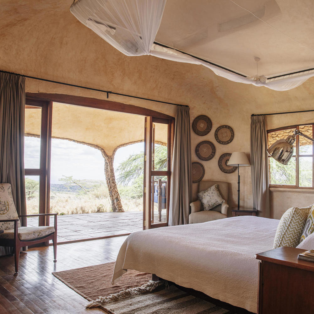 A bright safari lodge bedroom with a large bed, mosquito net, and open doors leading to an outdoor patio.