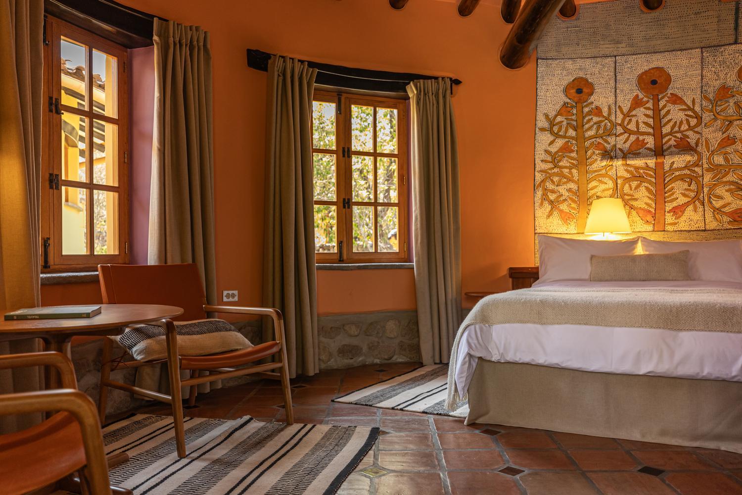 Bedroom interior with orange walls, rustic tile floors, a white bed, and a botanical tapestry.