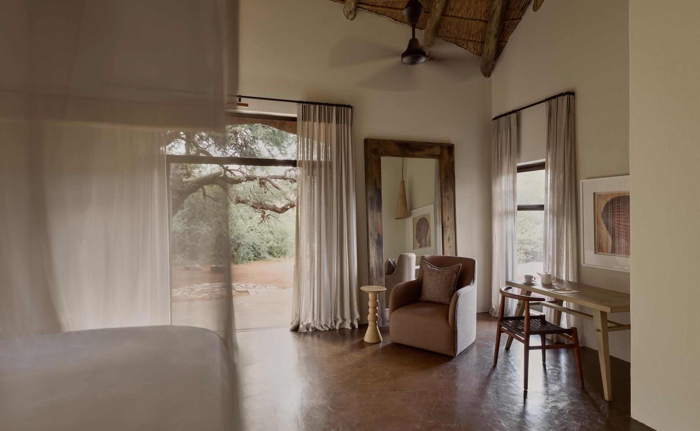 An interior bedroom view showing a cozy armchair, writing desk, and open door framed by light curtains.
