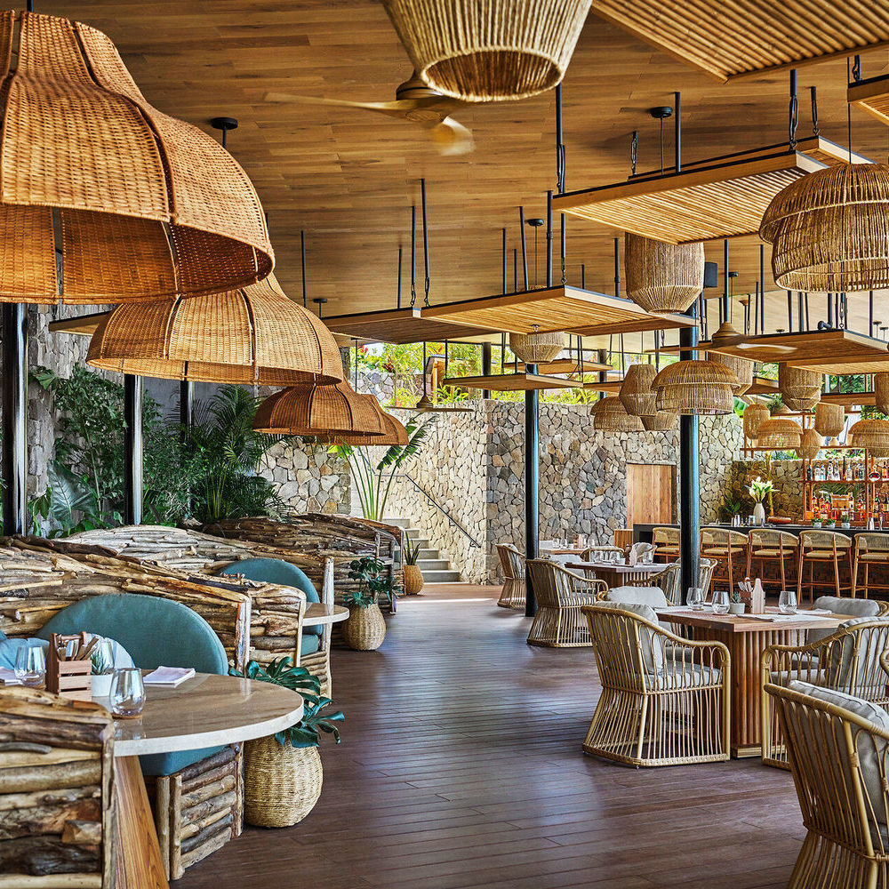 Elegant restaurant interior with large woven pendant lamps, wooden tables, and stone walls.