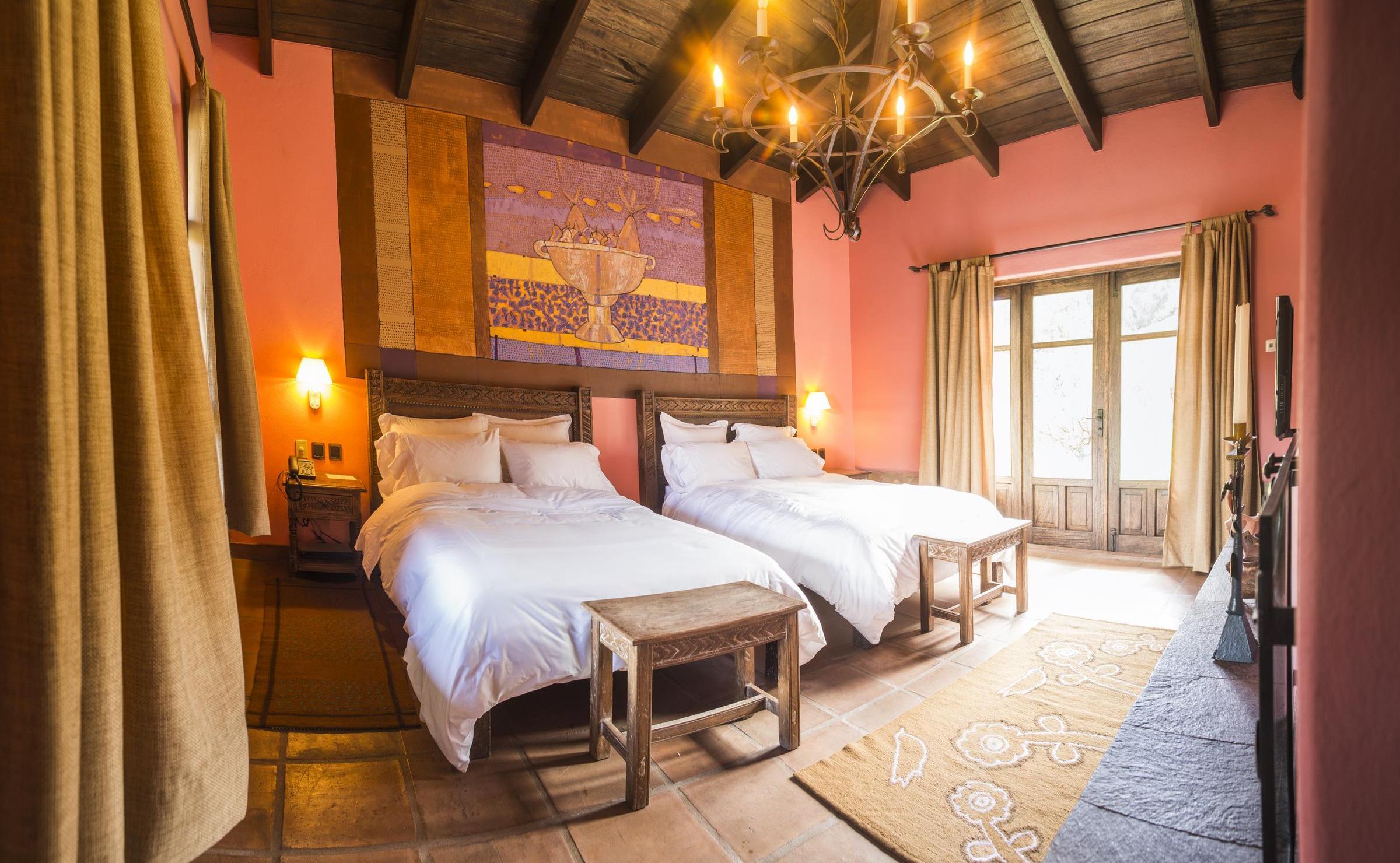 Hotel room featuring two beds with white linens, pink walls, and a large purple and gold tapestry.