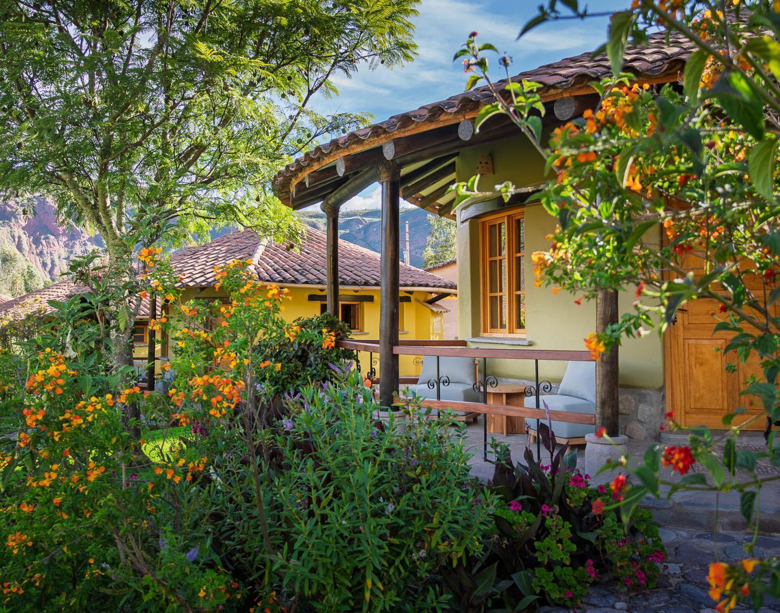 Yellow building with a tiled roof and wooden porch, surrounded by gardens with orange flowers.