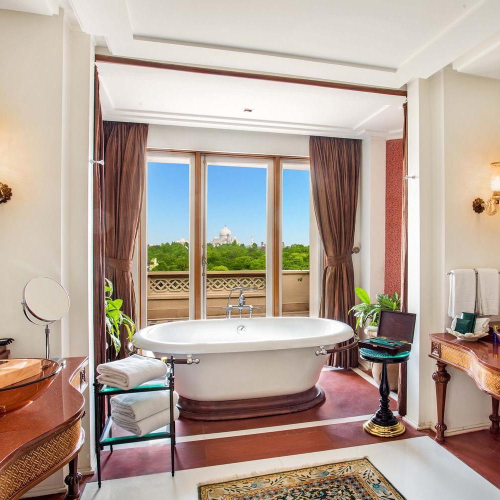 A white soaking tub in a luxury bathroom with a window view of the Taj Mahal in the distance