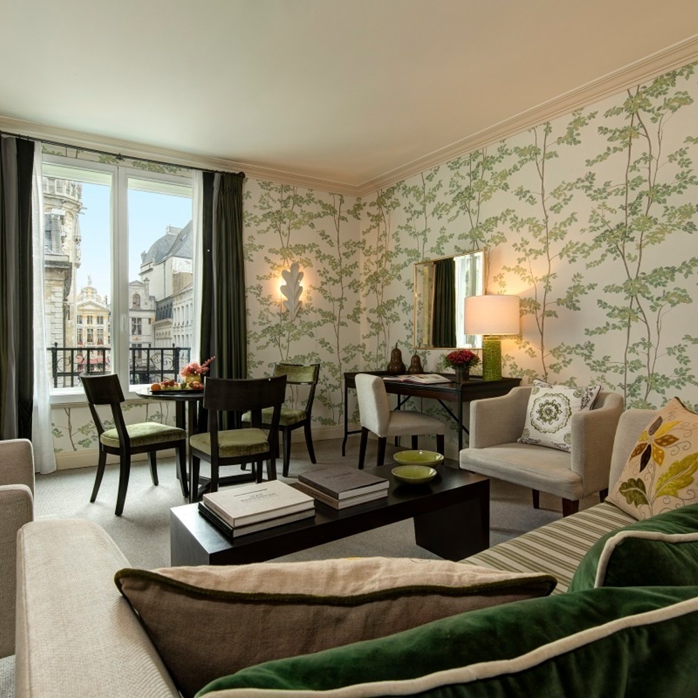 Cozy lounge area in the Prestige Suite at hotel amigo in belgium with leaf-patterned wallpaper and green velvet chairs.