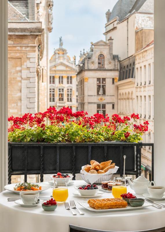 Breakfast table at hotel amigo in belgium looking through a window with red flowers toward historic city buildings.