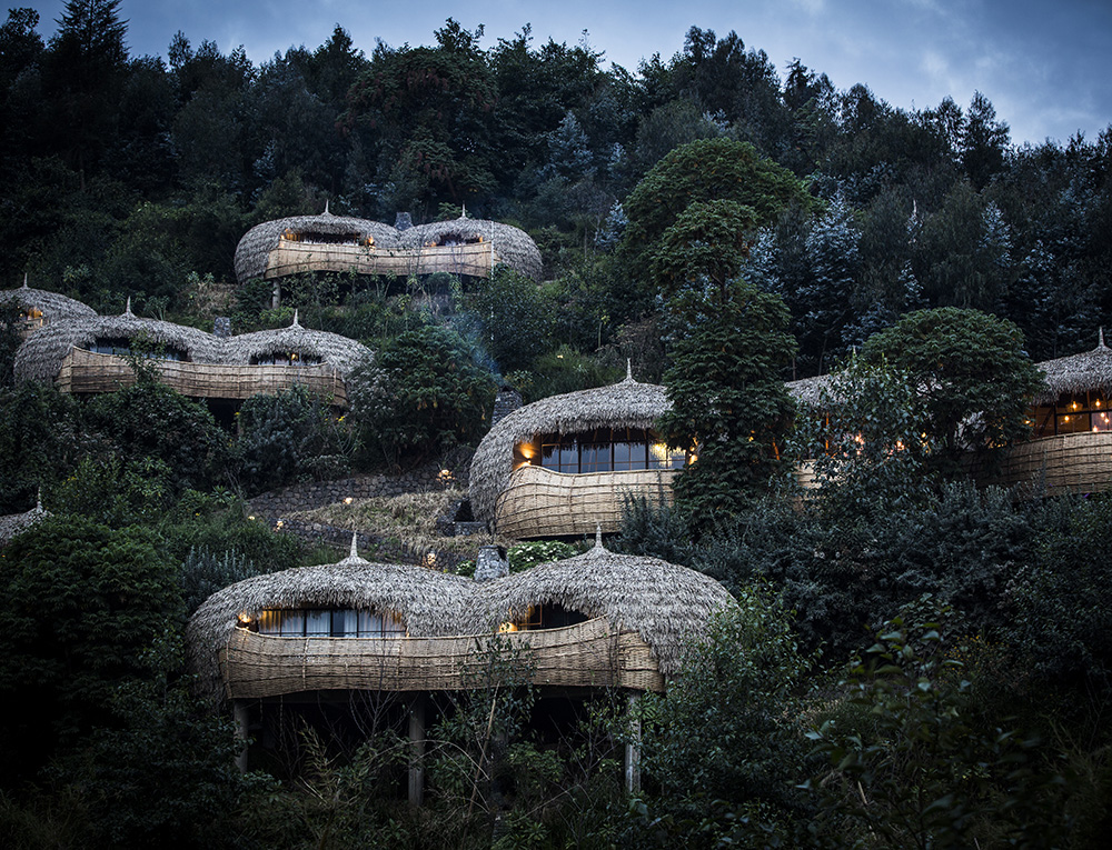 A hillside view of thatched-roof villas tucked away in thick green forest under a clear sky.