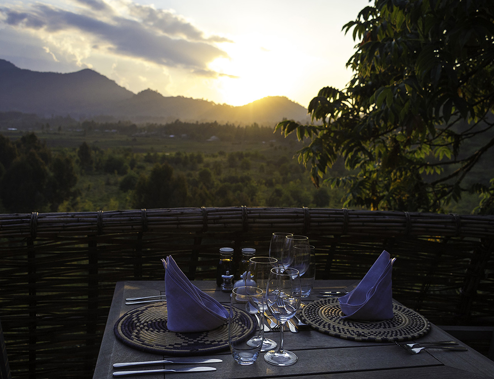 A formal dinner table setting on a wooden deck overlooking a mountain valley during a golden sunset.